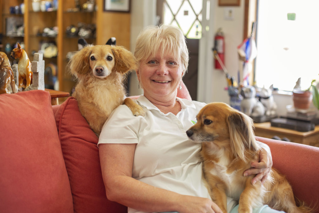 two dogs sit with female owner on red couch