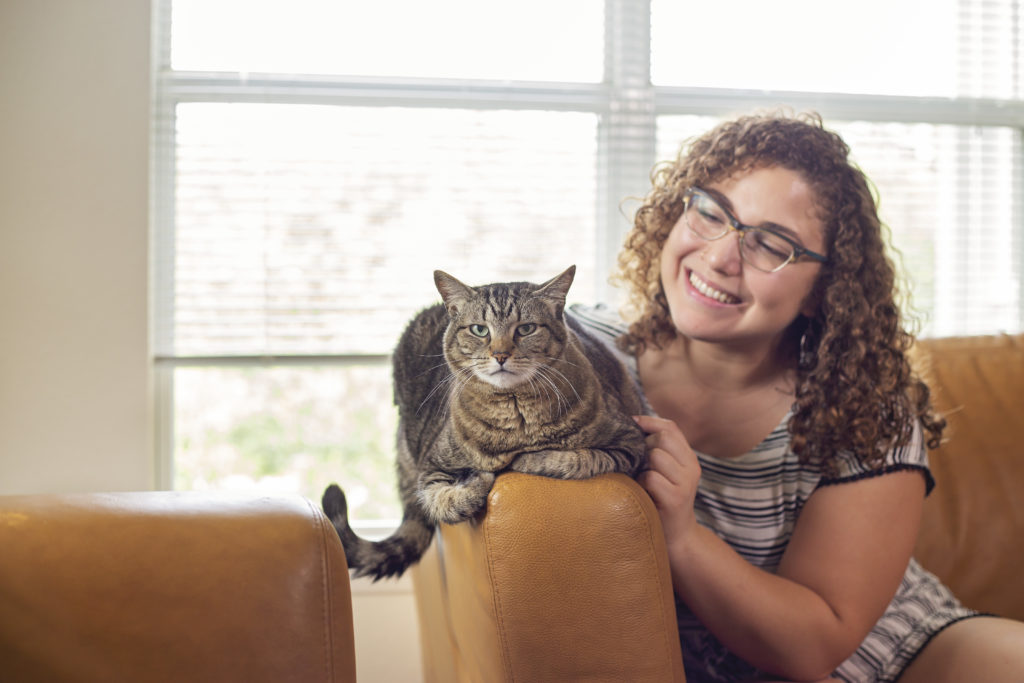 A girl sits in a chair looking lovingly at her cat that is on the arm rest